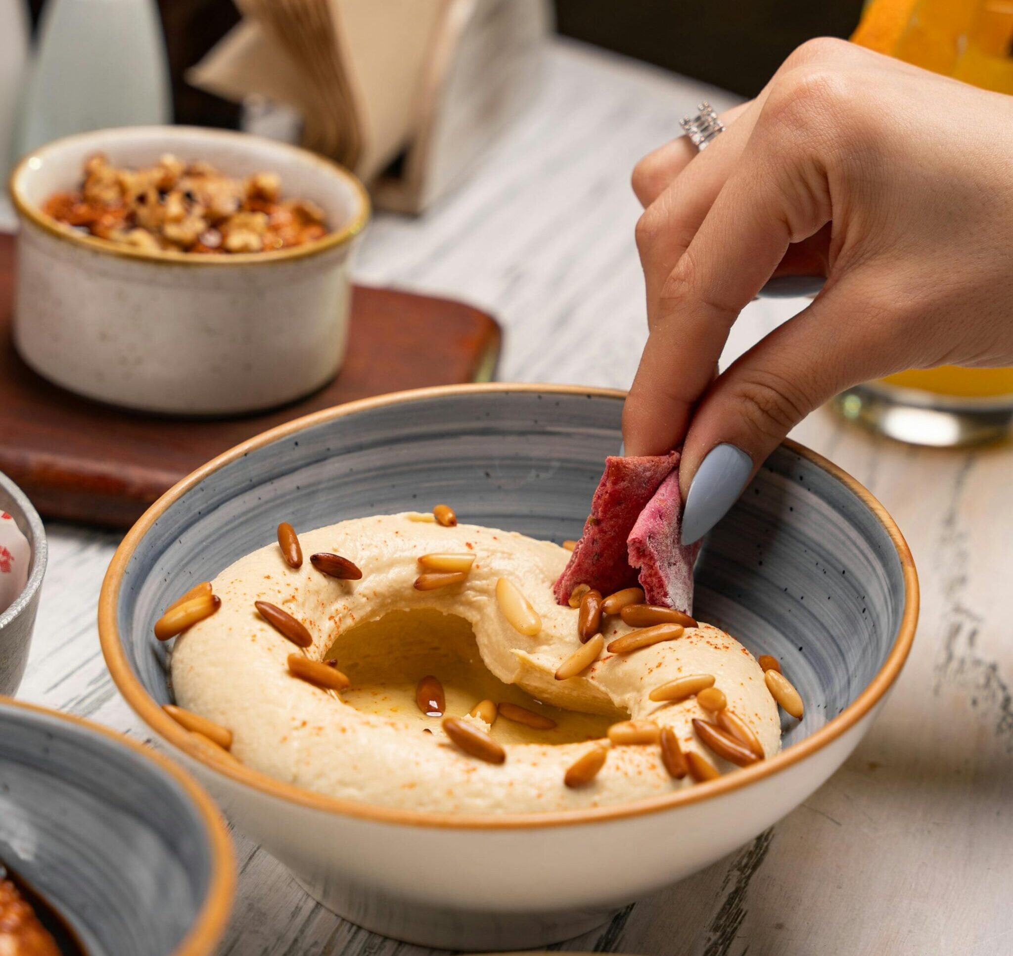 Close-up of a hand dipping bread into hummus topped with pine nuts, capturing a delicious Mediterranean meal.