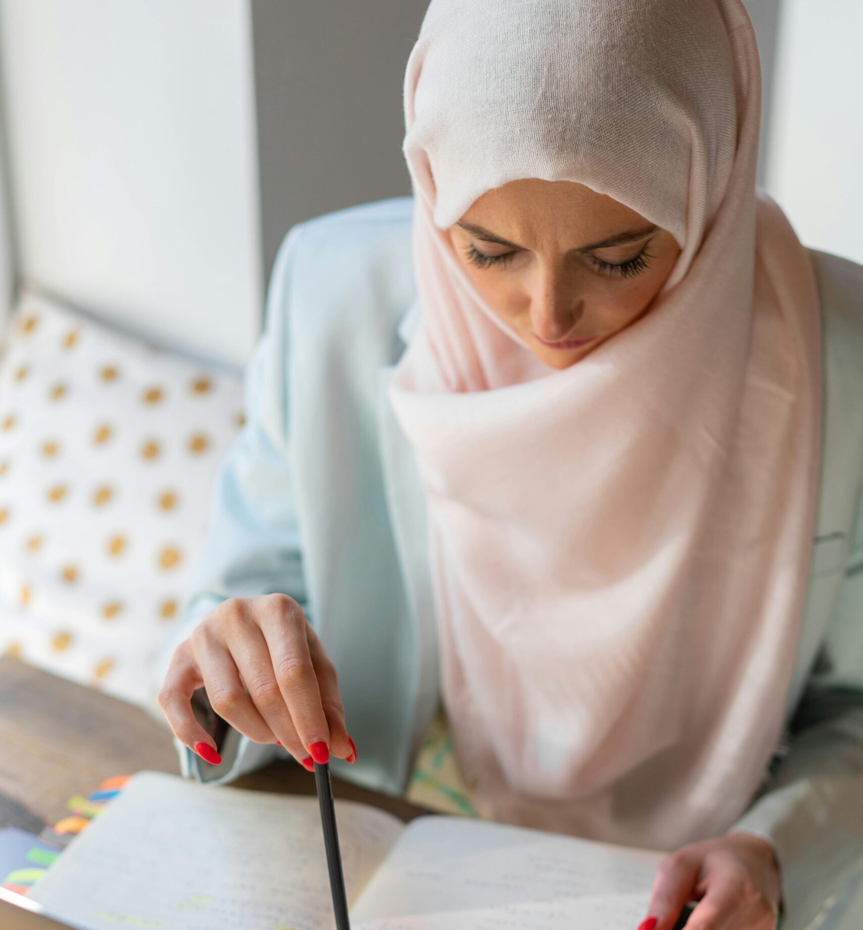 Middle Eastern woman in hijab studying with laptop and notepad indoors.